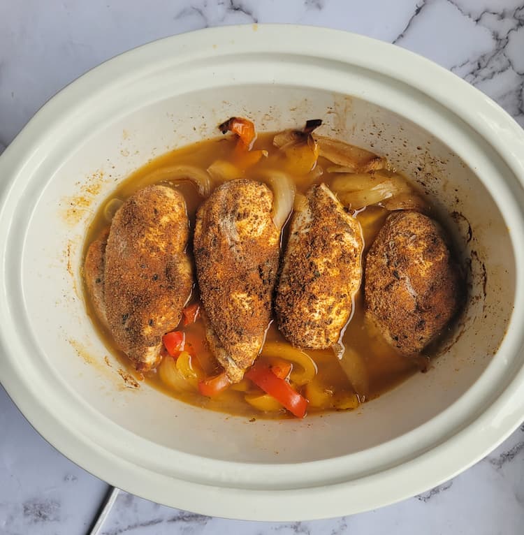 crockpot with 4 cooked seasoned chicken breasts over sliced peppers and onions in chicken broth
