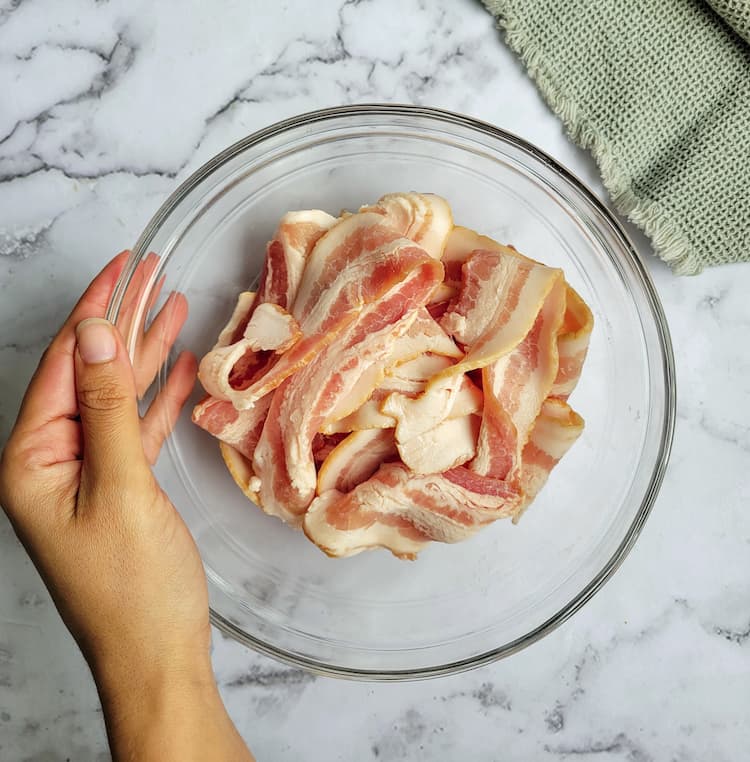 hand holding a bowl of raw bacon strips