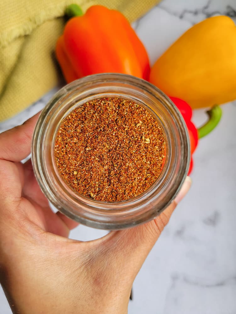 hand holding a jar of spices over a red, yellow and orange pepper