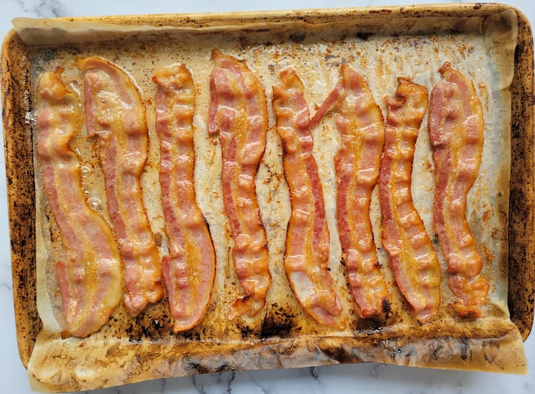 cooked strips of bacon on a parchment lined baking sheet