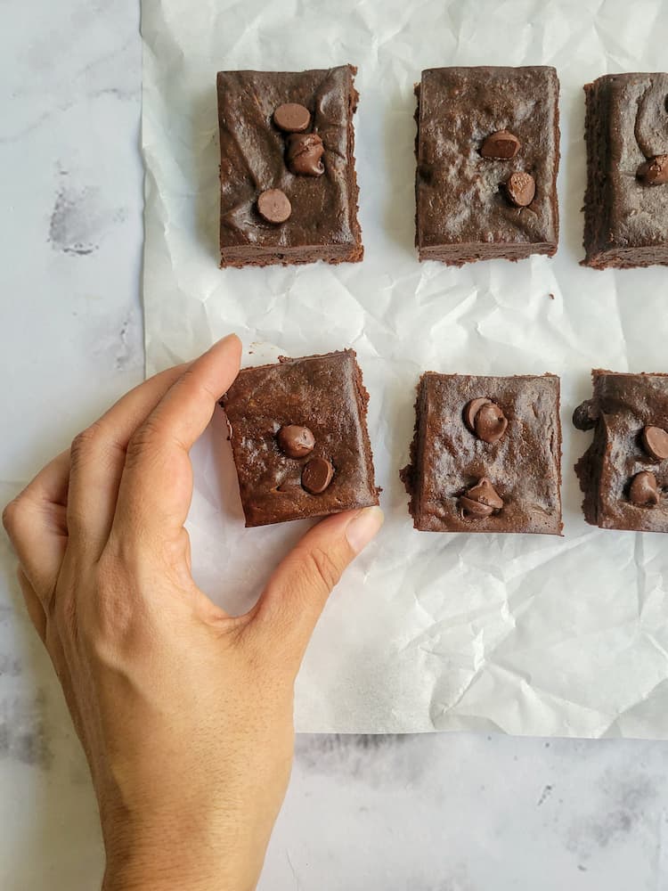 hand grabbing a brownie next to 5 others on a piece of parchment paper