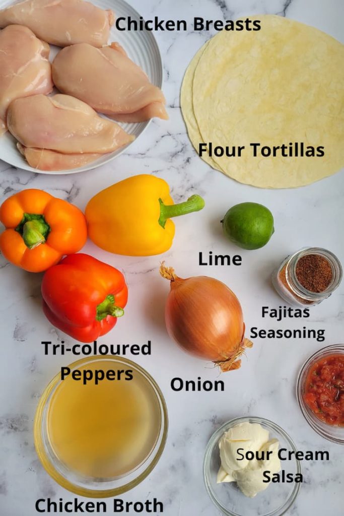 ingredients for chicken fajitas in crockpot - chicken breasts, flour tortillas, tri-coloured peppers, sour cream, salsa, fajitas seasoning, onion, chicken broth, lime