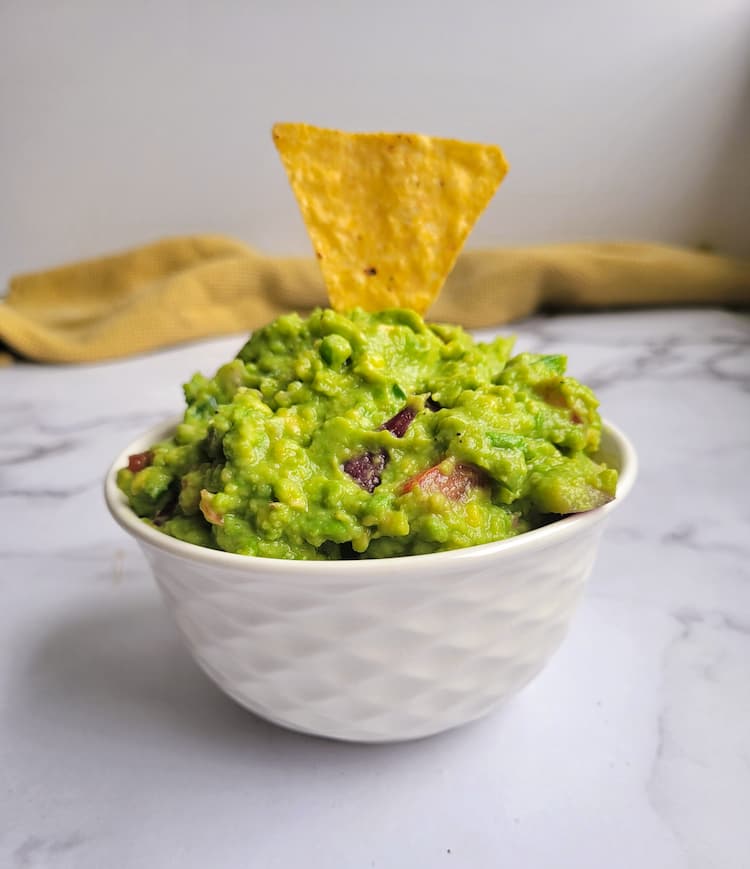 bowl of guacamole with a tortilla chip dunked in on top
