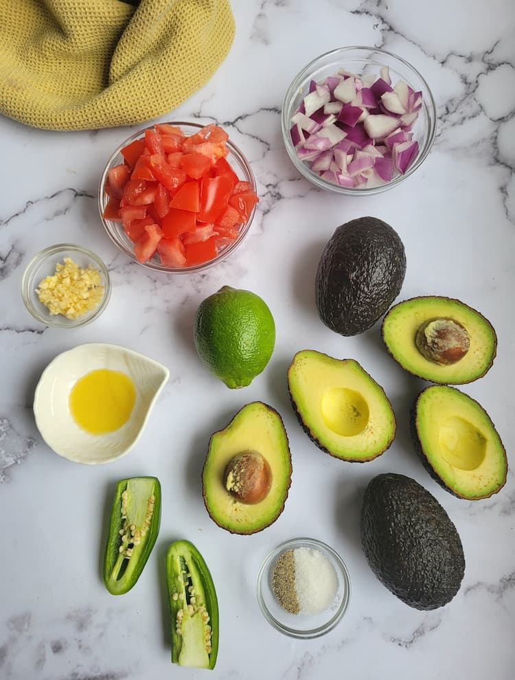 ingredients for recipe for easy guacamole - avocados, tomatoes, red onions, jalapeno, garlic, salt and pepper, olive oil