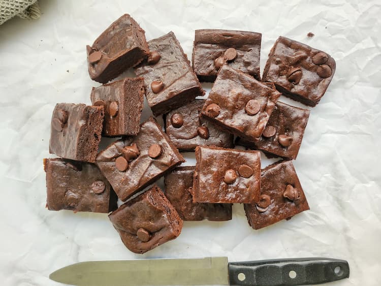 pile of avocado brownies topped with chocolate chips on a piece of parchment paper next to a knife