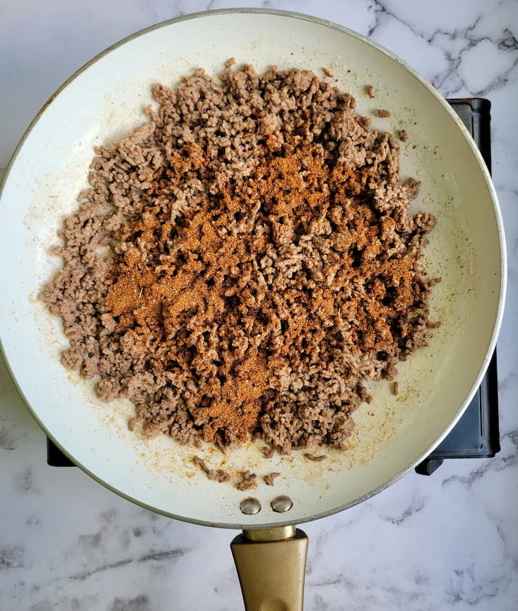 skillet with cooked ground beef and seasonings