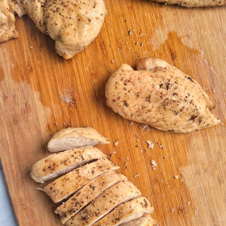 4 cooked juicy chicken breasts on a cutting board, one sliced into pieces