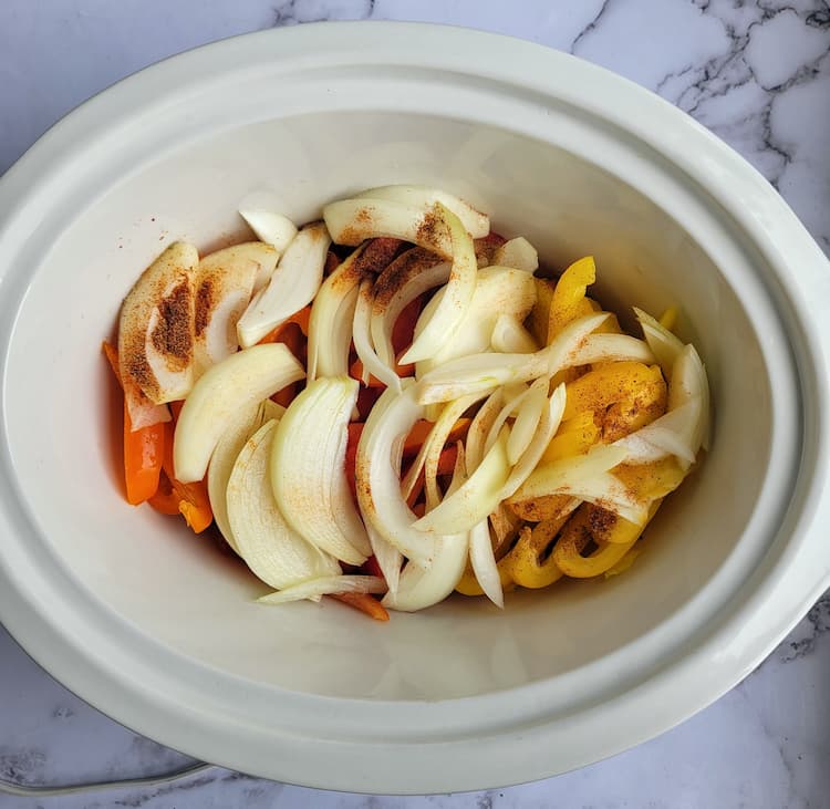 crockpot of sliced white onions and peppers with seasoning on top