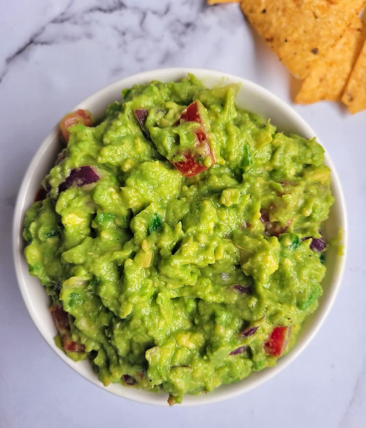 bowl of guacamole with tortilla chips in the background