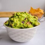 bowl of guacamole with tortilla chips in the background