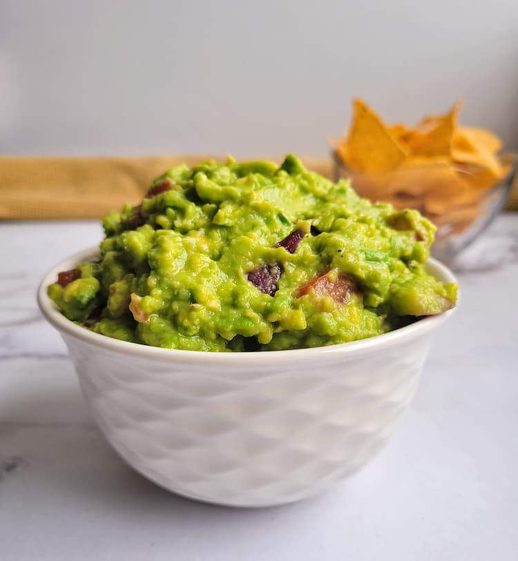 bowl of guacamole with tortilla chips in the background
