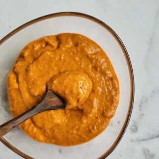 bowl of thai peanut sauce with a wooden spoon in it and tips of chopsticks in the background