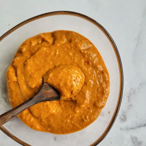 bowl of thai peanut sauce with a wooden spoon in it and tips of chopsticks in the background