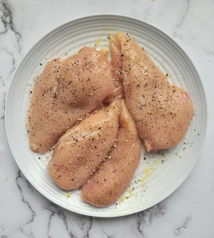 plate with 4 raw chicken breasts seasoned with salt and pepper