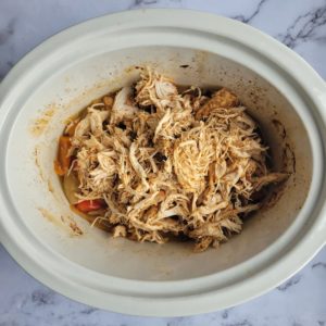 crockpot of cooked shredded chicken over sliced peppers