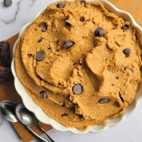 bowl of chickpea cookie dough with chocolate chips, two spoons and 3 dates on the side