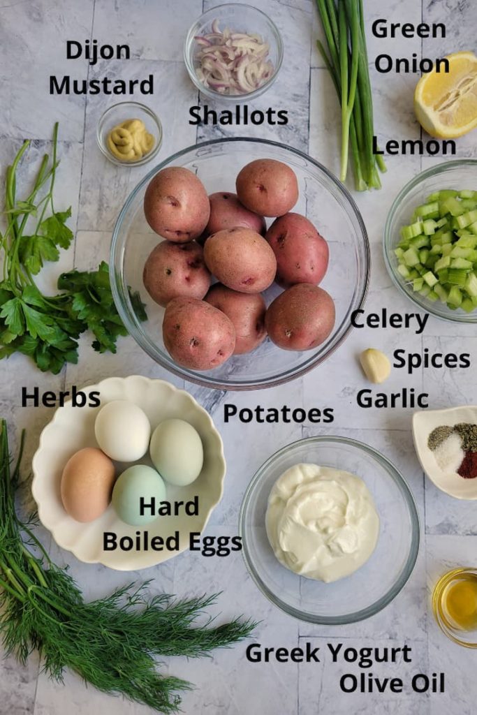 ingredients for the best potato salad - red skinned potatoes, dijon mustard, greek yogurt, lemon, hard boiled eggs, olive oil, spices, celery, garlic, green onion, shallots and fresh herbs