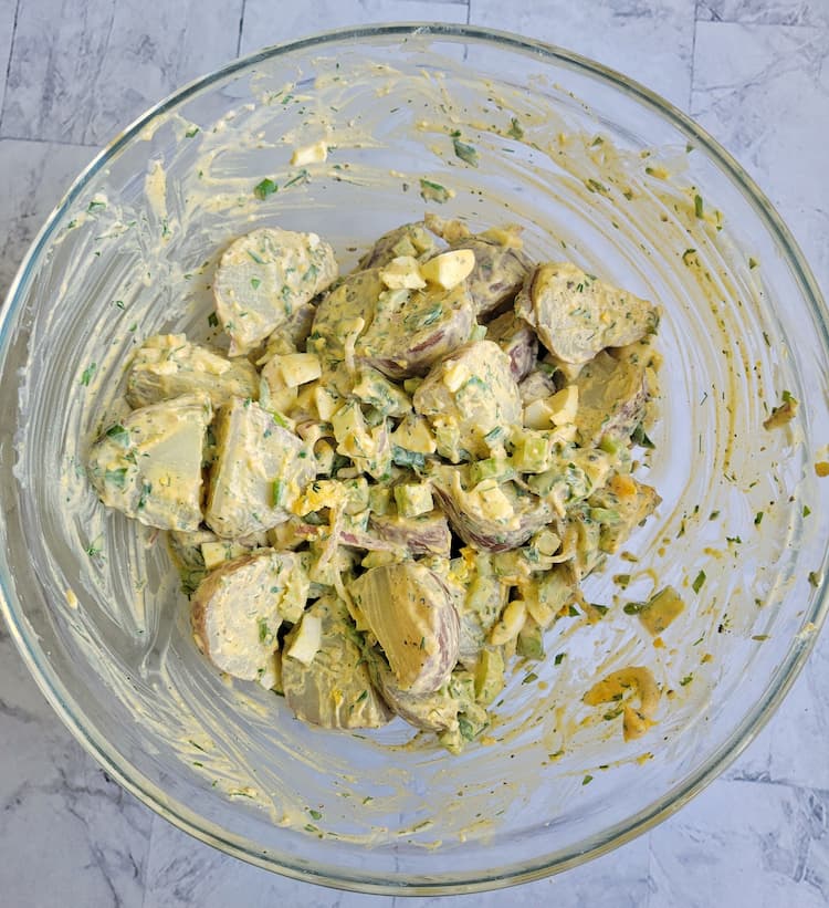 bowl of halved potatoes mixed with herbs, hard boiled eggs and other ingredients in a creamy dressing