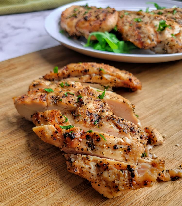 sliced grilled chicken breast on a cutting board, plate with more in the background