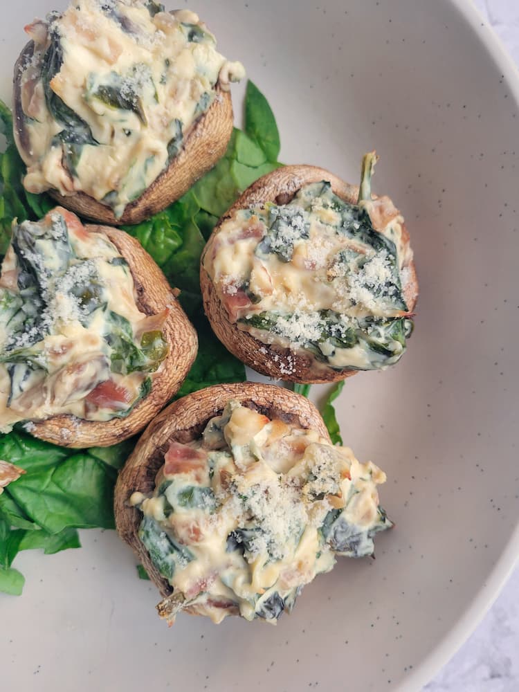 close up shot of 4 creamy stuffed mushrooms with spinach and bacon