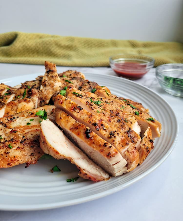 plate of sliced grilled chicken, ramekins of red sauce and parsley in the background
