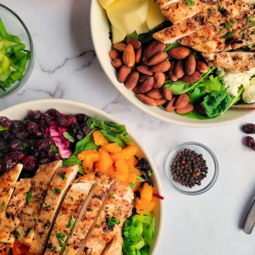 two salads with grilled chicken, ramekin of peppercorns, green onions and carrots around