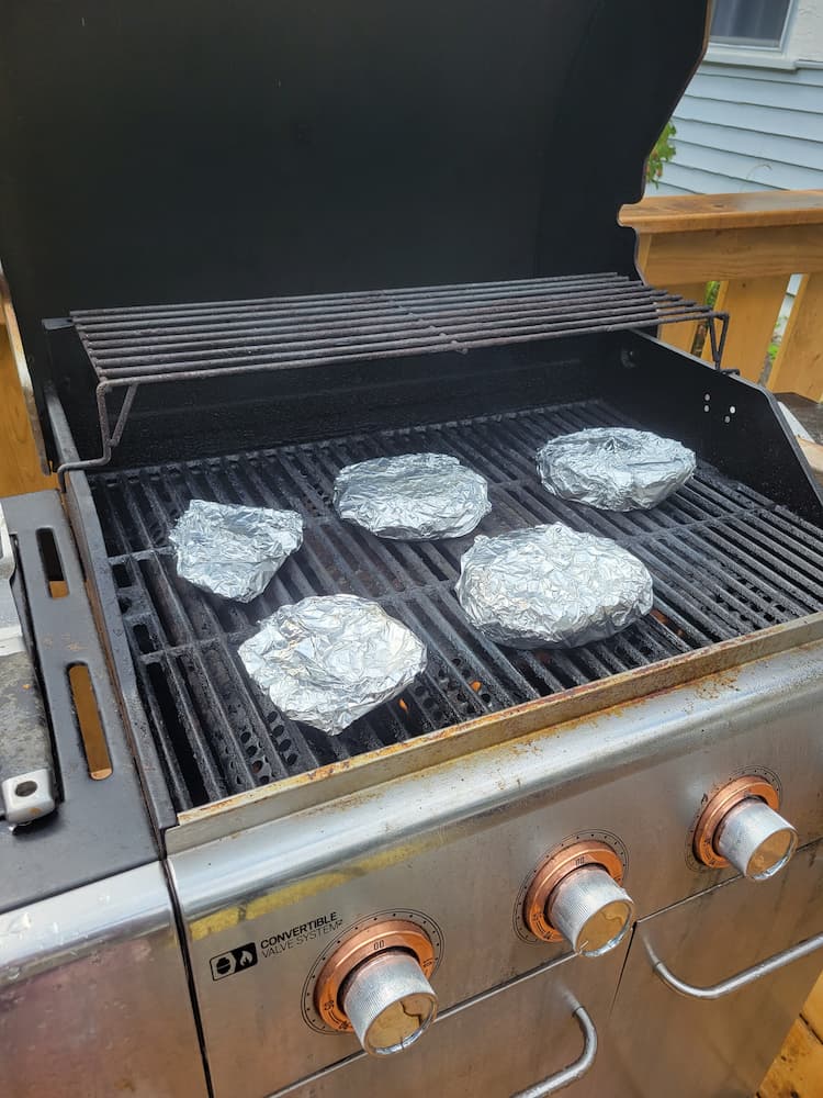 5 cabbage steaks wrapped in aluminum foil on a bbq