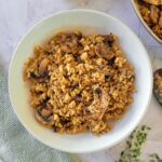 bowl of mushroom risotto, fresh sprigs of thyme at the bottom, ramekin of parmesan cheese and another bowl of risotto cut off at the top