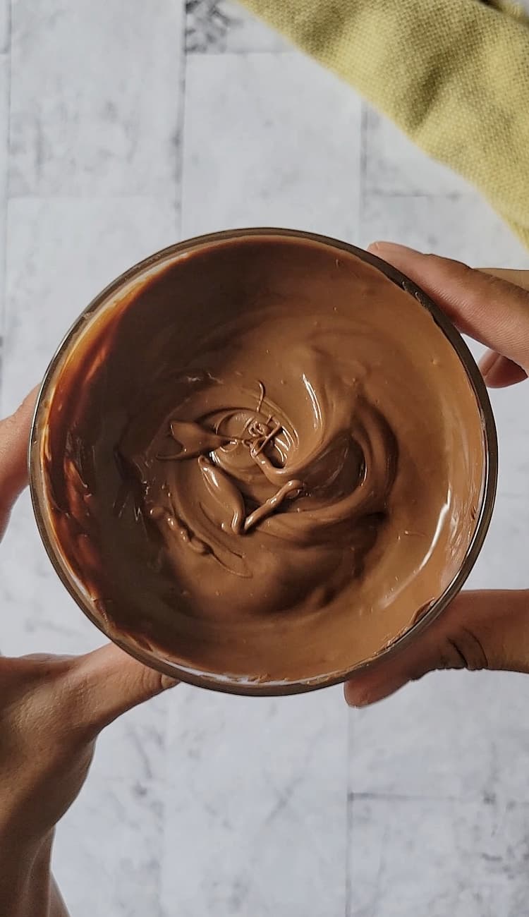 two hands holding up a small bowl of melted chocolate