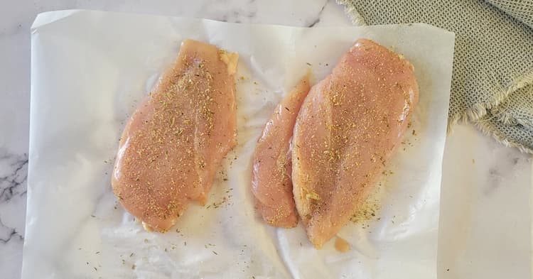 2 raw seasoned chicken breasts on parchment paper