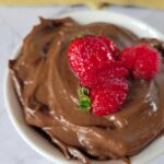 close up of a bowl of chocolate mousse made from avocado with 3 sliced strawberries on top