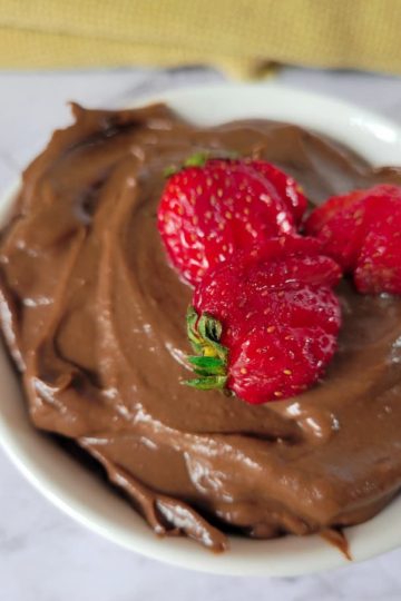 close up of a bowl of chocolate mousse made from avocado with 3 sliced strawberries on top