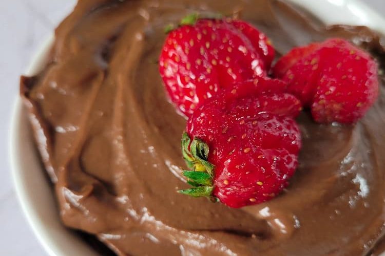 close up of a bowl of chocolate mousse made from avocado with 3 sliced strawberries on top