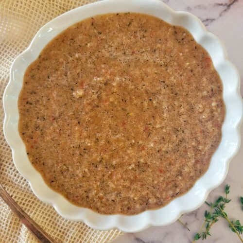close up of a bowl of jerk sauce, fresh herbs in the background