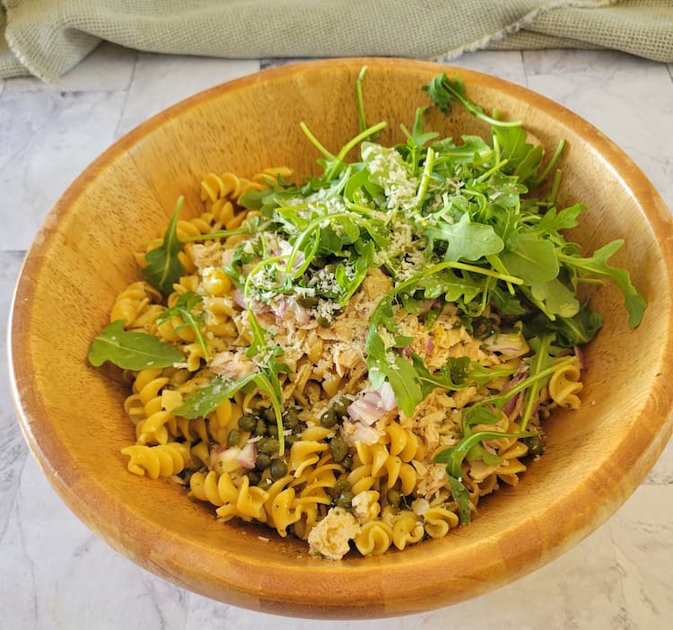 wooden bowl with curly pasta, arugula, shallots, capers, tuna and parmesan cheese