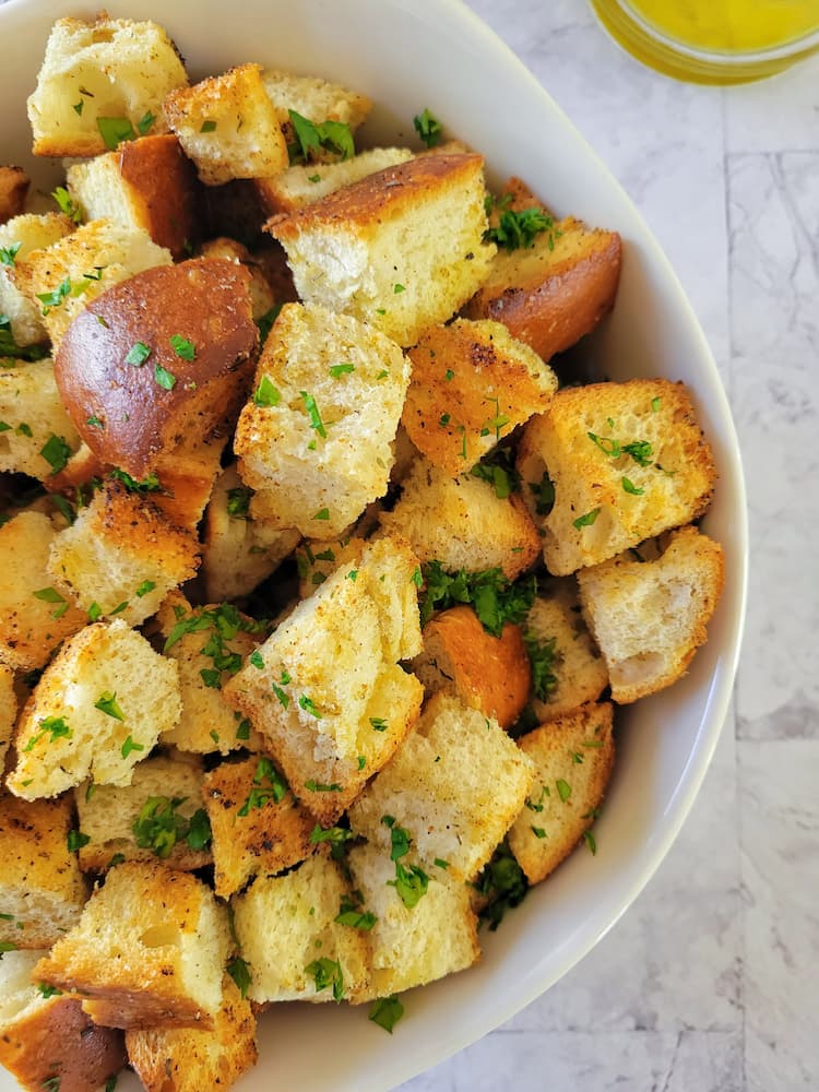 a bowl of croutons garnished with fresh chopped parsley, olive oil in the background