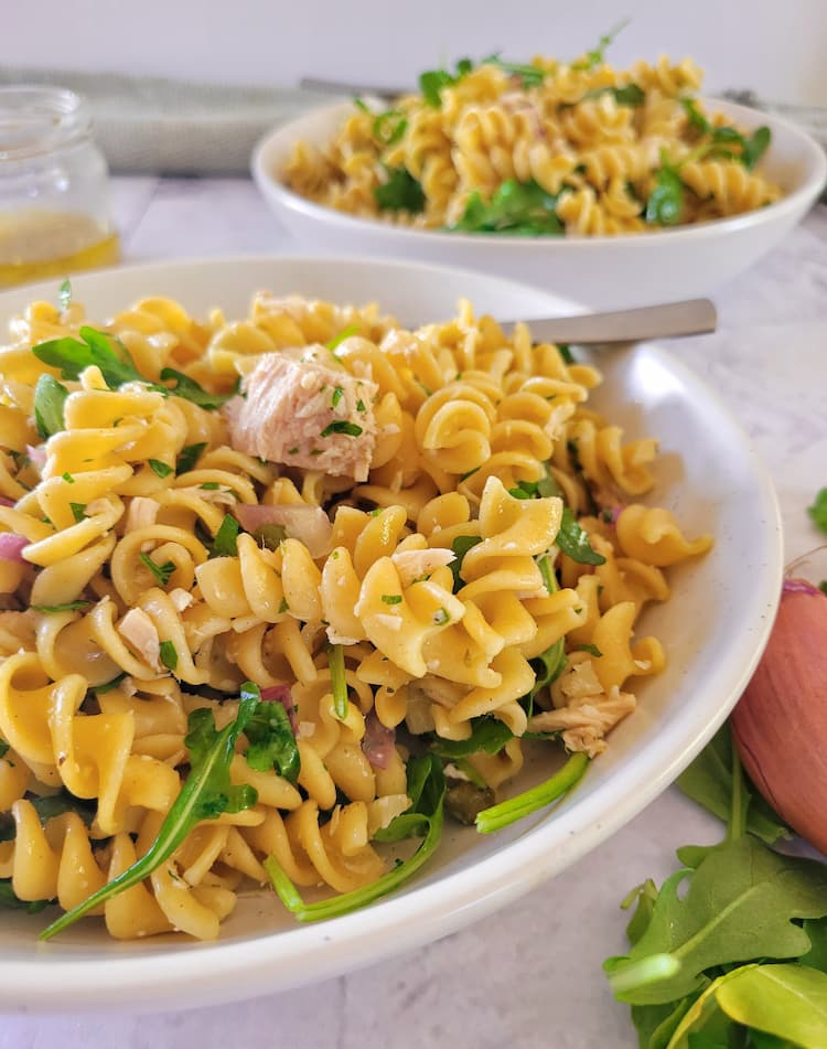 close up of a bowl of pasta salad with tuna and arugula, another bowl in the background