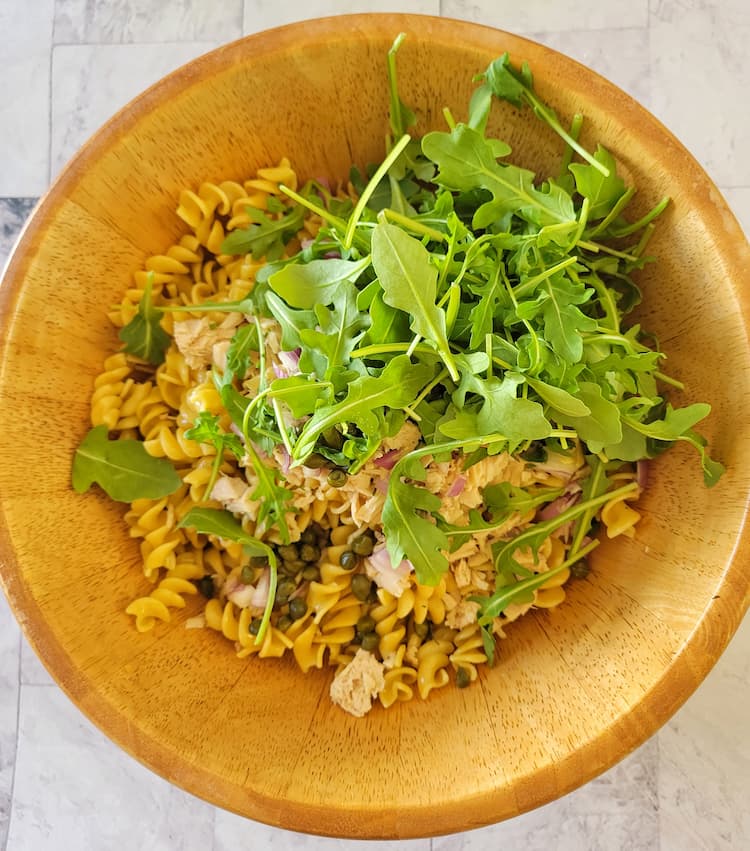 wooden bowl with curly pasta, arugula, shallots, capers, tuna