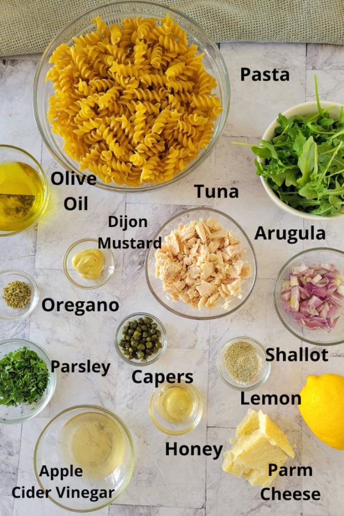ingredients for pasta salad with tuna - pasta, arugula, tuna, shallots, lemon, parmesan cheese, honey, capers, parsley, apple cider vinegar, dijon mustard, oregano, olive oil