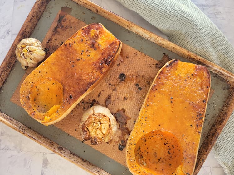sheet pan with two roasted butternut squash halves and two roasted garlic bulbs
