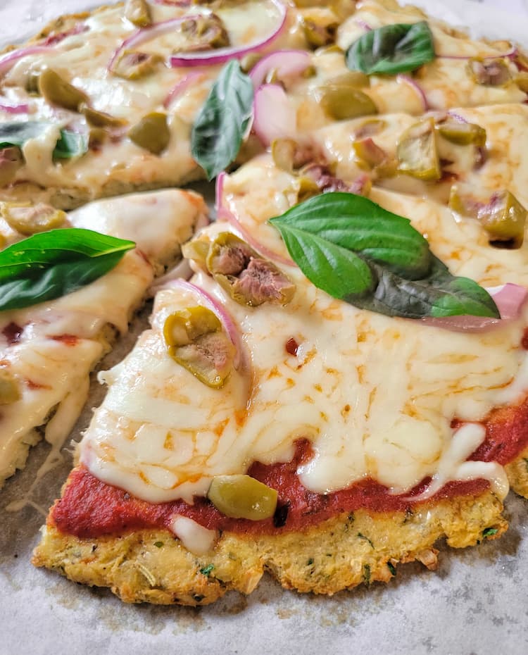 close up of a cauliflower crust pizza topped with mozzarella cheese, fresh basil, tomato sauce, green olives and red onion
