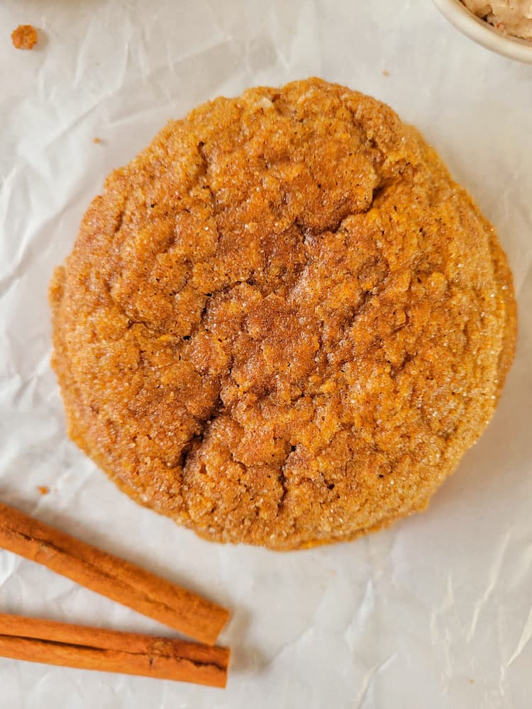 close up of a pumpkin spice cookie next to two cinnamon sticks