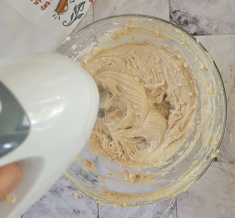 hand with an electric mixer mixing frosting in a bowl