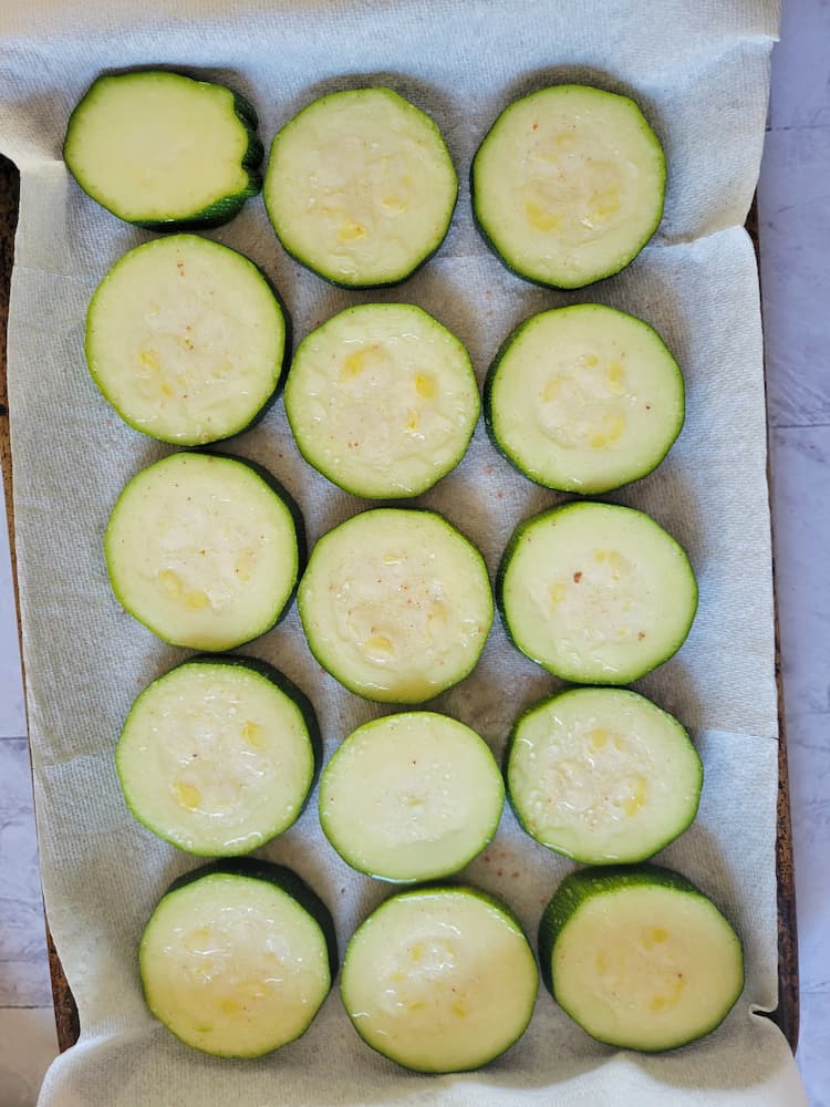 parchment lined baking sheet with salted zucchini rounds releasing their moisture