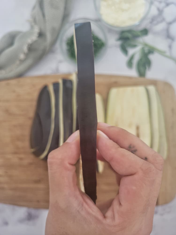 hand holding a piece of sliced eggplant over a cutting board with the rest