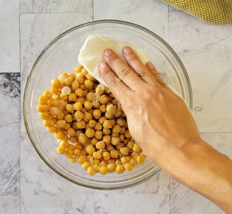 hand with a paper towel patting chickpeas in a bowl