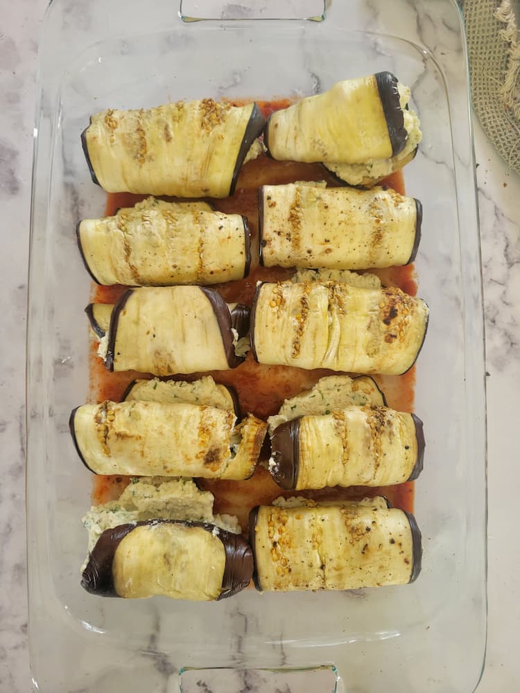 glass baking dish with eggplant rollatini on tomato sauce