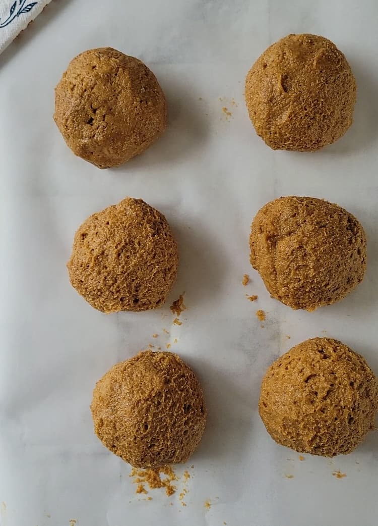 parchment lined baking sheet with 6 large cookie dough balls dipped in cinnamon sugar (pre-bake)