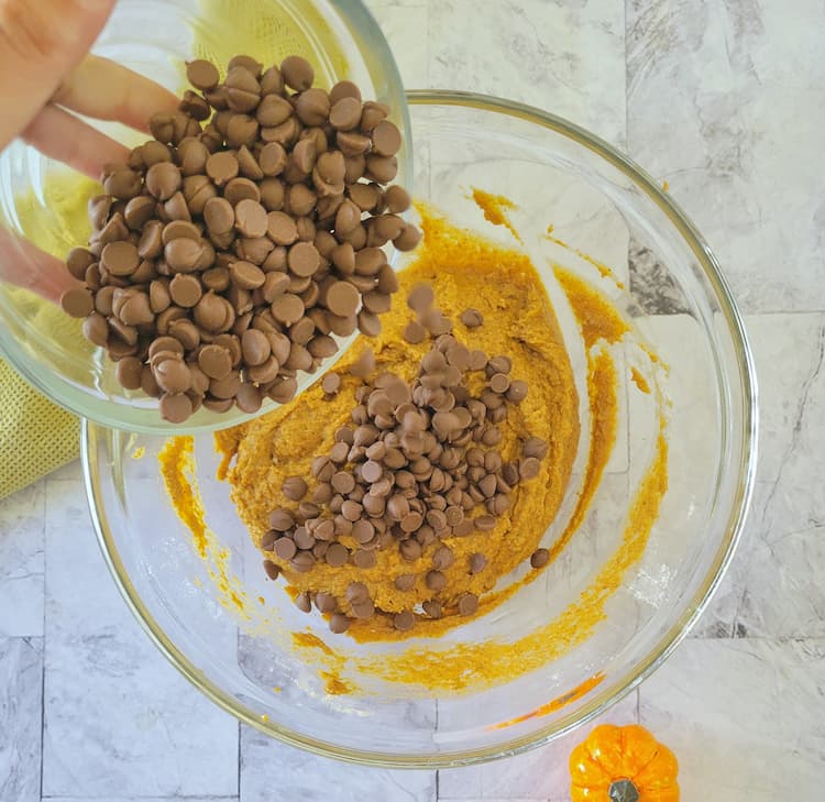 chocolate chips being poured into a bowl of orange batter