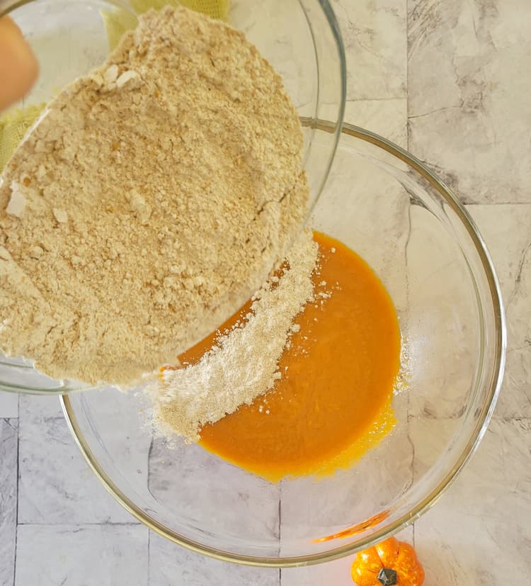 bowl of flour being added to a bowl of orange batter